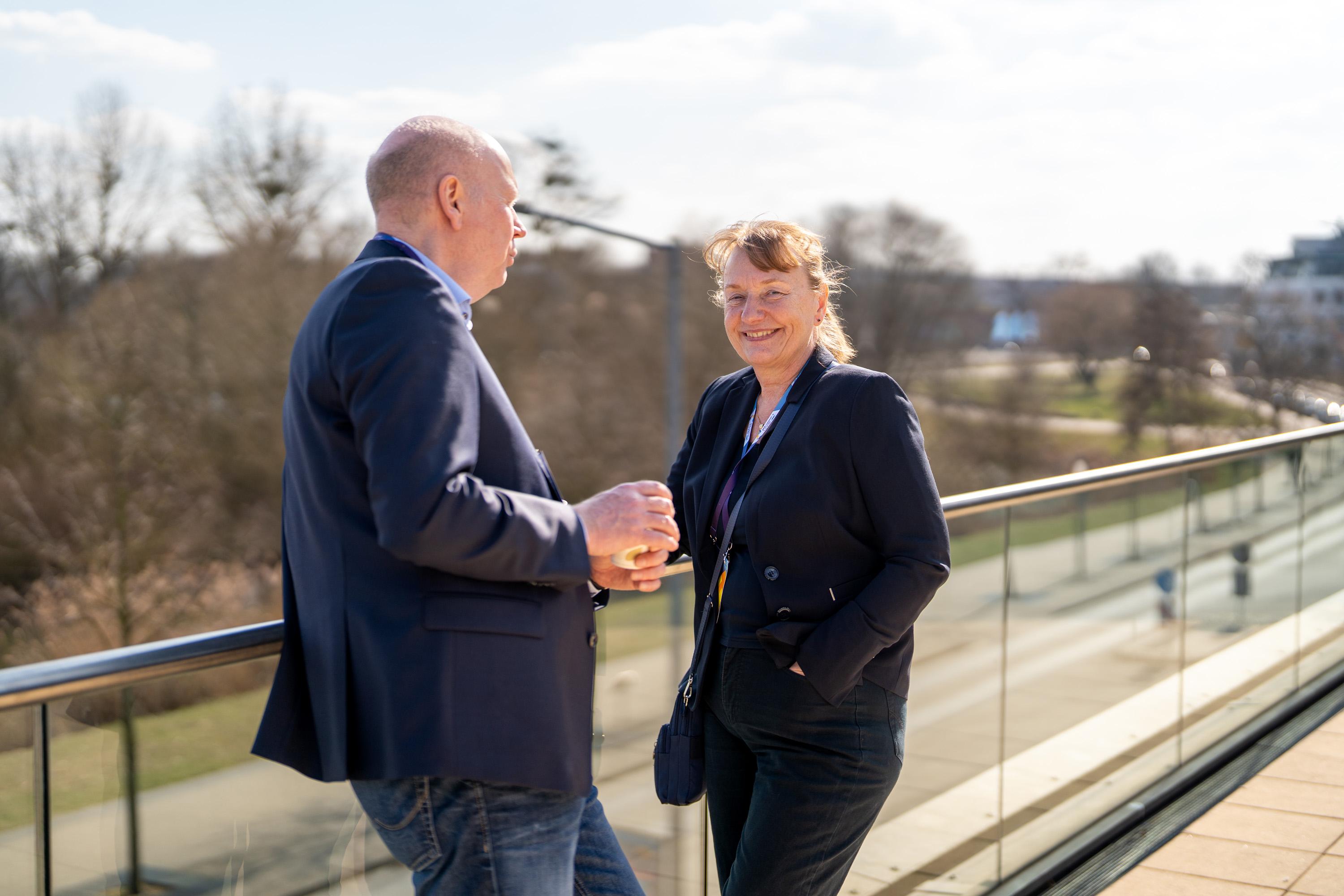 Uta Knöchel steht mit einem Mann in Anzug auf der Dachterrasse der IHK zu Schwerin. Sie unterhalten sich.