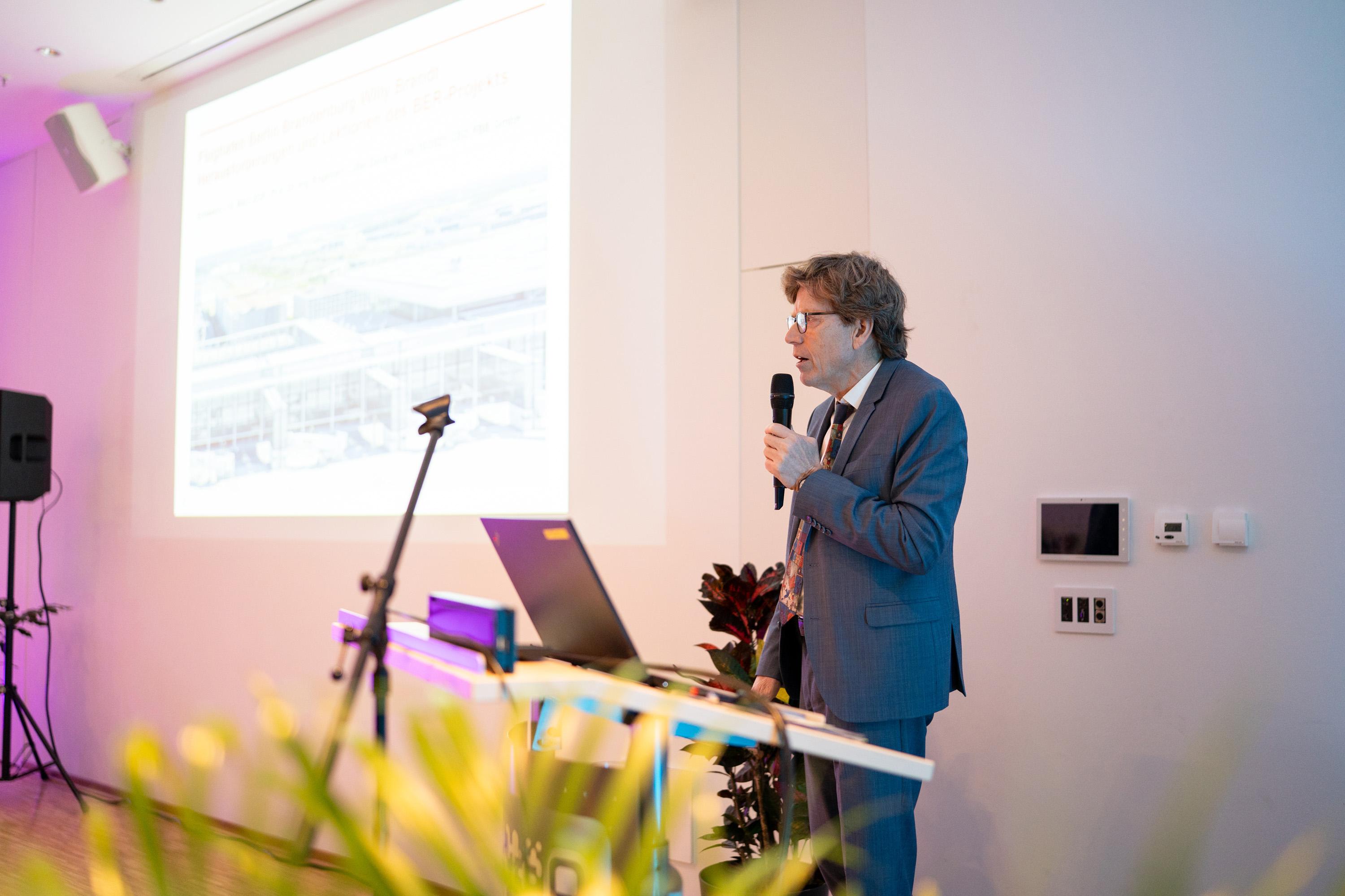 Prof. Dr. Engelbert Lütke Daldrup spricht am Rednerpult mit Laptop, im Hintergrund eine Präsentation auf Leinwand.