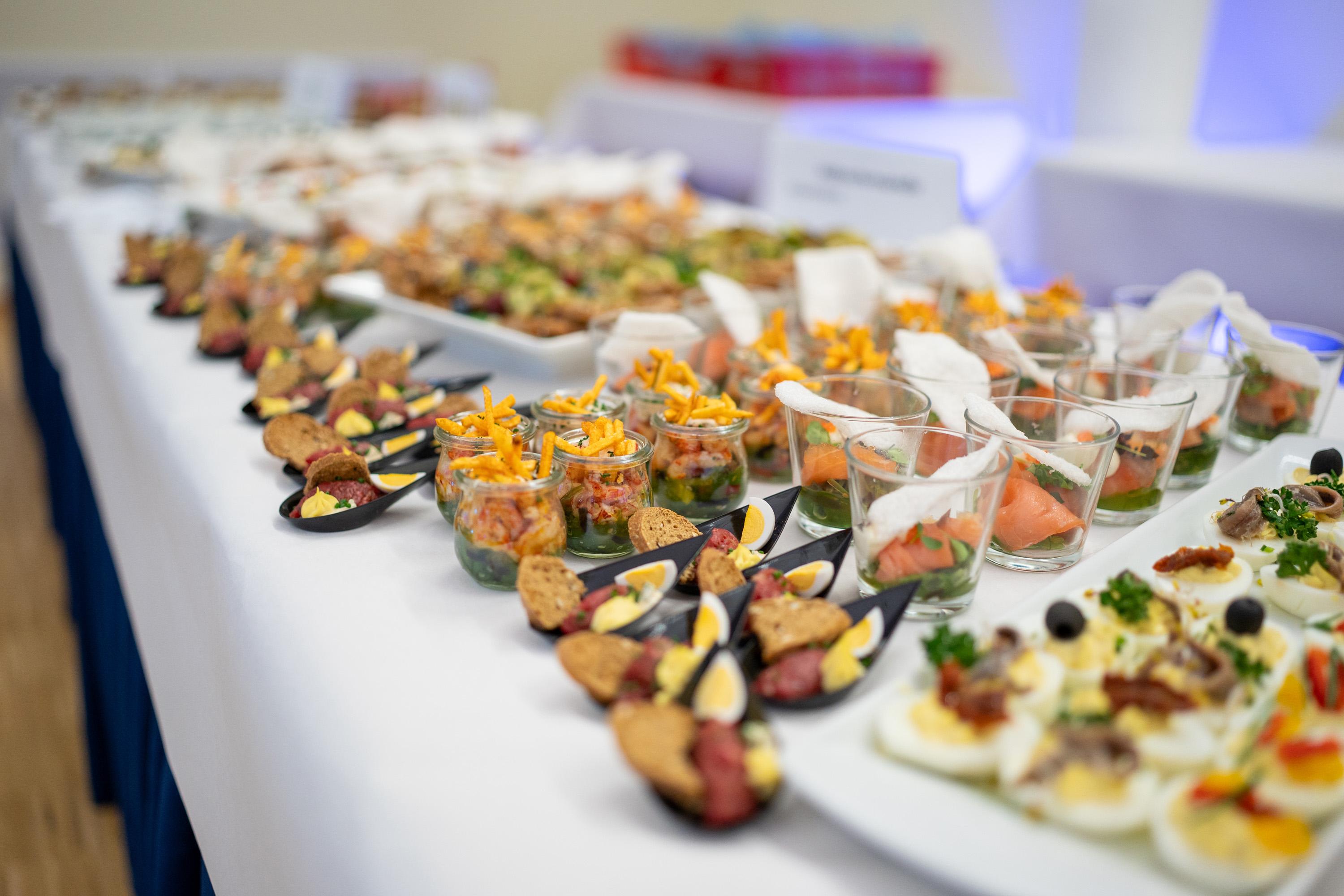 Buffet mit verschiedenen Fingerfood-Optionen, darunter gefüllte Gläser, Häppchen auf Löffeln und dekorierte Platten.